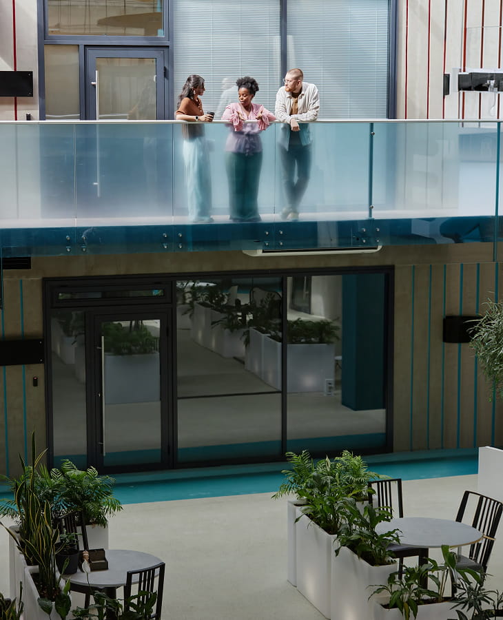 Three founders talking on a glass mezzanine above the workspace.